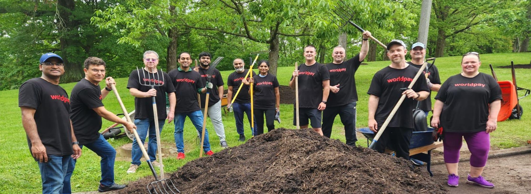 A group of people wearing black t-shirts with red text reading ‘Worldpay’, holding gardening equipment and standing in a field.